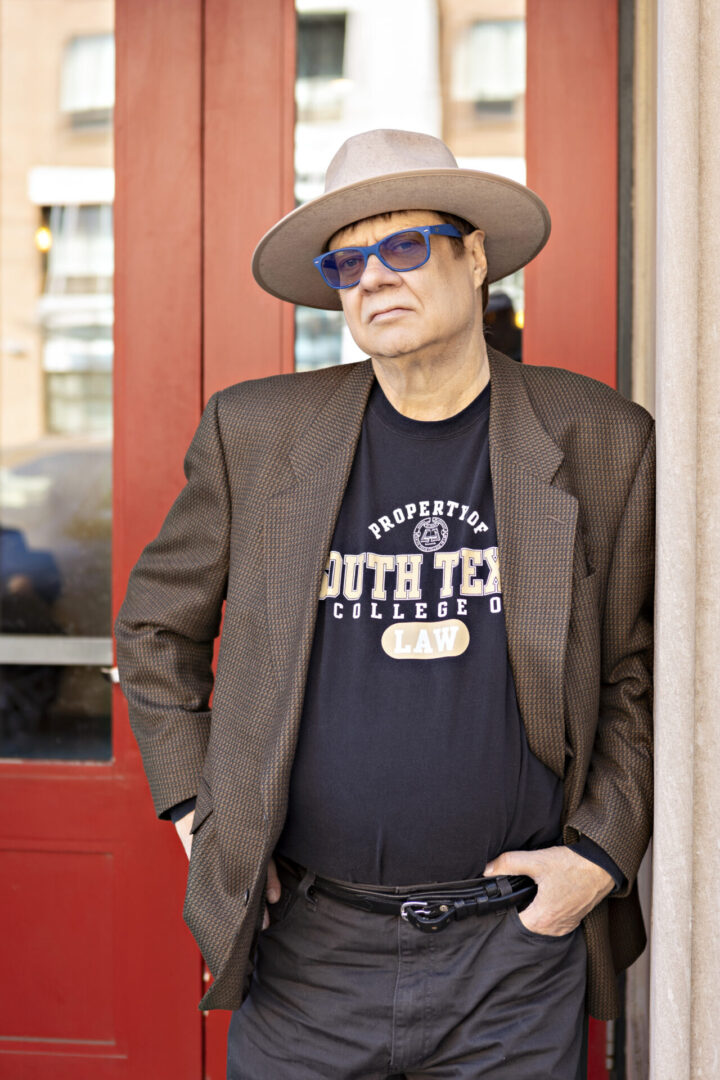 A man in a hat and sunglasses standing outside.